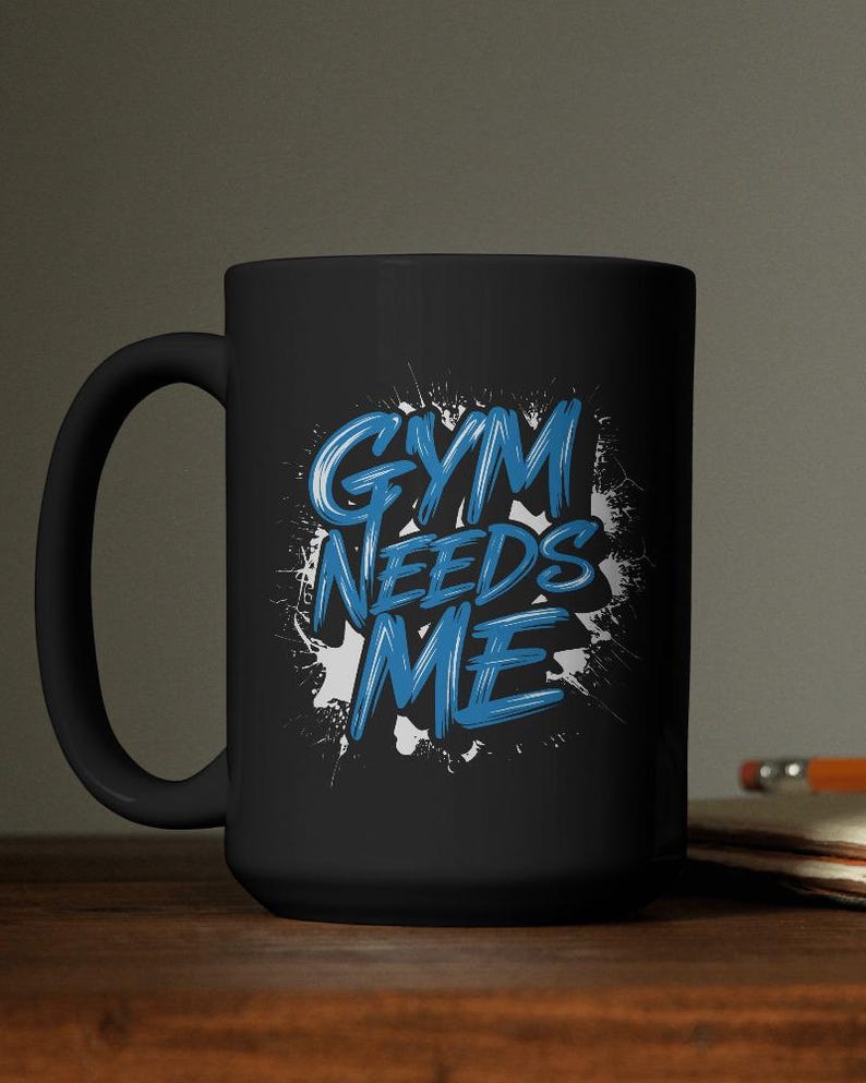May include: Black ceramic mug with the text "GYM NEEDS ME" in blue, stylized lettering. The text is set against a white splatter design. The mug has a curved handle and is suitable for hot or cold beverages.