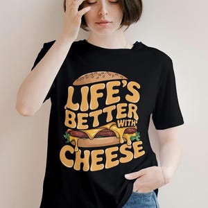 Pu&ograve; includere: Maglietta nera con un'immagine di un cheeseburger e il testo "Life's Better With Cheese".