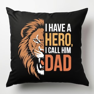 Puede incluir: Almohada negra con la cabeza de un le&oacute;n en el lado izquierdo y el texto "Tengo un h&eacute;roe, lo llamo pap&aacute;" en el lado derecho.