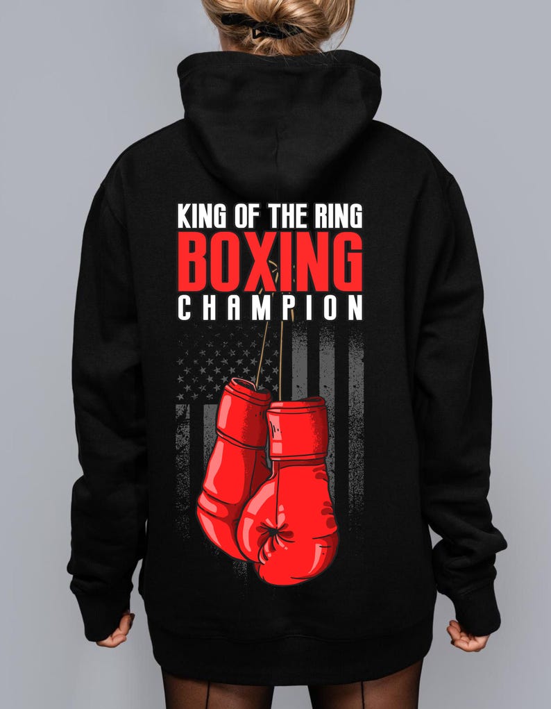 Peut inclure: Sweat-shirt &agrave; capuche noir avec le texte "King of the Ring Boxing Champion" et un graphique de gants de boxe rouges devant un drapeau am&eacute;ricain.