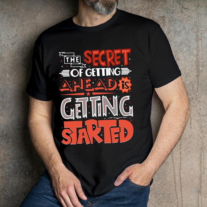 May include: Black t-shirt with the quote "THE SECRET OF GETTING AHEAD IS GETTING STARTED" in red and white lettering. The shirt has a crew neck and short sleeves. The design is centered on the chest.