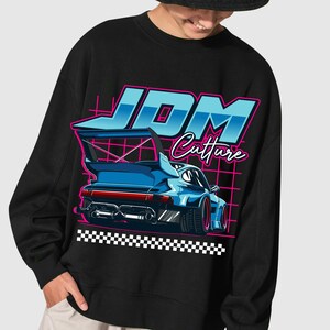 Puede incluir: Sudadera negra con un gr&aacute;fico de un coche deportivo azul con un aler&oacute;n grande. El texto "JDM Culture" est&aacute; en azul y rosa. Un patr&oacute;n de cuadros est&aacute; en la parte inferior del gr&aacute;fico.