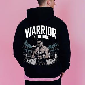 Peut inclure: Sweat-shirt &agrave; capuche noir avec un imprim&eacute; graphique d'un boxeur dans un ring. Le texte "Warrior in the Ring" est imprim&eacute; au-dessus du graphique.
