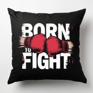 Peut inclure: Un oreiller noir avec du texte blanc qui dit "Born to Fight" et un graphique de deux gants de boxe rouges.