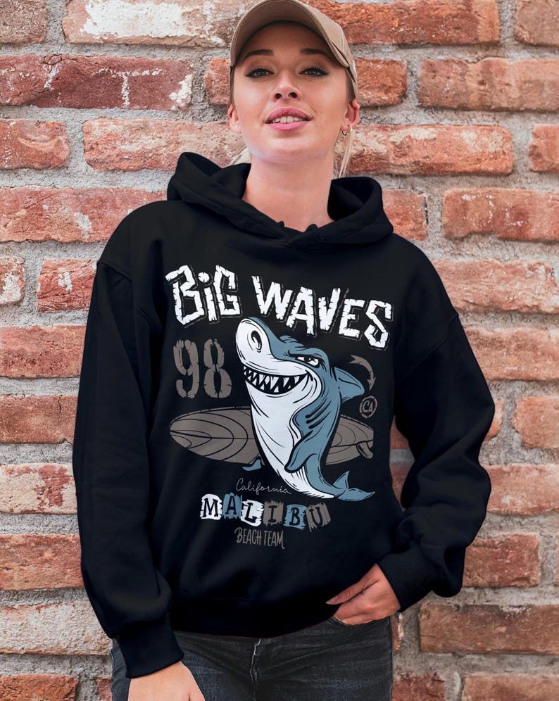May include: Black hooded sweatshirt featuring a graphic of a shark riding a surfboard. The graphic includes the text "Big Waves 98 California Malibu Beach Team".