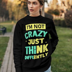 May include: Black sweatshirt with the text "I'M NOT CRAZY JUST THINK DIFFERENTLY" in yellow and teal lettering. The sweatshirt is a crew neck style and is being worn outdoors.