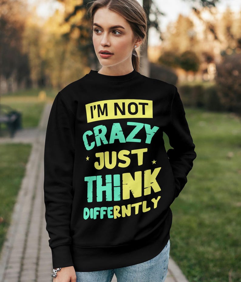 May include: Black sweatshirt with the text "I'M NOT CRAZY JUST THINK DIFFERENTLY" in yellow and teal lettering. The sweatshirt is a crew neck style and is being worn outdoors.