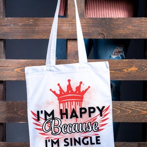 May include: White tote bag with a red crown and the text "I'm Happy Because I'm Single" printed on it.