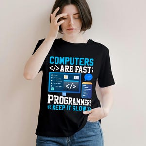 Puede incluir: Camiseta negra con un gr&aacute;fico azul y blanco. El gr&aacute;fico dice "COMPUTERS ARE FAST; PROGRAMMERS KEEP IT SLOW" con s&iacute;mbolos de ordenador y codificaci&oacute;n. La camiseta es de cuello redondo.