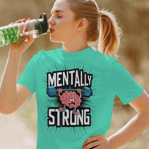 May include: A turquoise t-shirt with the words "MENTALLY STRONG" in a bold, black font. The design features a cartoon brain lifting weights. The person in the image is drinking from a water bottle.