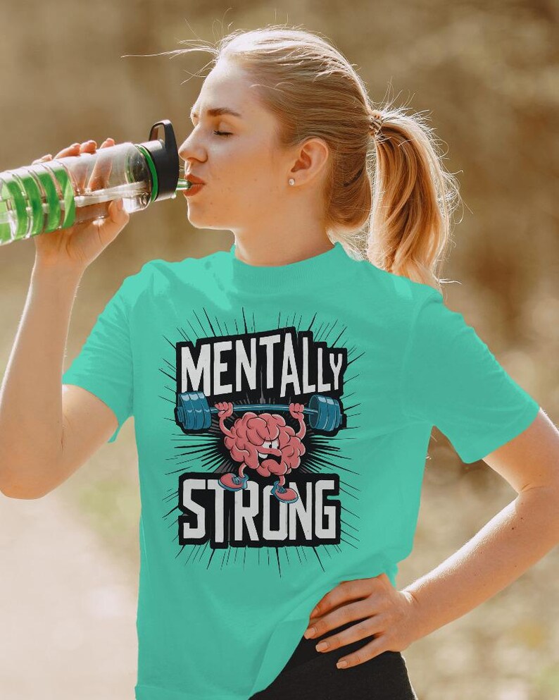 May include: A turquoise t-shirt with the words "MENTALLY STRONG" in a bold, black font. The design features a cartoon brain lifting weights. The person in the image is drinking from a water bottle.