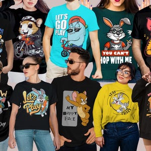 May include: A collection of graphic t-shirts and sweatshirts featuring cartoon characters. Designs include a penguin fishing, a hamster on a motorcycle, a blue monster on a bike, a rabbit with a carrot, and a cat with a fishing rod.