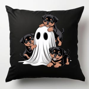 May include: Black throw pillow featuring a Halloween-themed design. Three Rottweiler puppies playfully interact with a white ghost. The puppies have black and brown fur, and the ghost has large, black eye holes. The background is solid black.