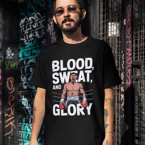 Peut inclure: T-shirt noir avec un imprim&eacute; graphique blanc d'un boxeur dans un ring de boxe. Le texte "BLOOD, SWEAT, AND GLORY" est imprim&eacute; sur le t-shirt.