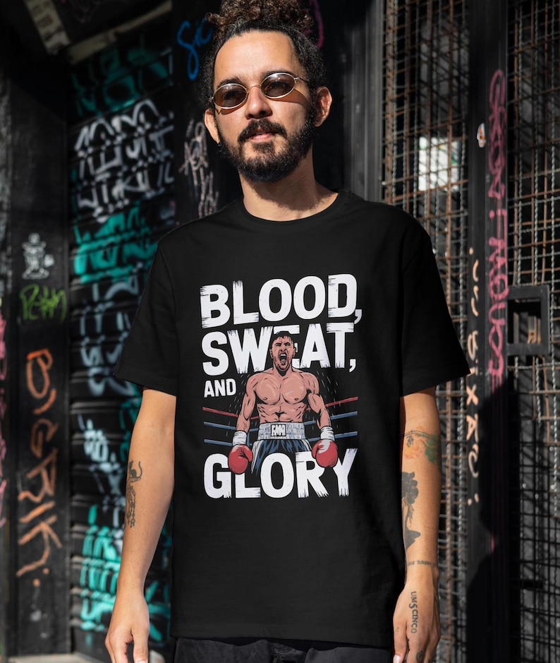 Peut inclure: T-shirt noir avec un imprim&eacute; graphique blanc d'un boxeur dans un ring de boxe. Le texte "BLOOD, SWEAT, AND GLORY" est imprim&eacute; sur le t-shirt.