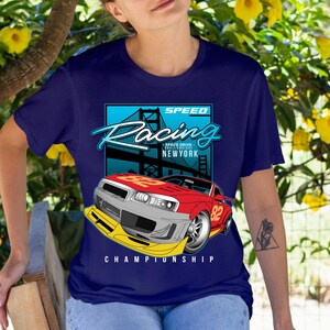 Puede incluir: Camiseta azul marino con un dise&ntilde;o de coche de carreras rojo y gris con el n&uacute;mero 82. El dise&ntilde;o incluye las palabras "SPEED Racing" y "NEWYORK" con una ilustraci&oacute;n de un puente. La palabra "CHAMPIONSHIP" est&aacute; en la parte inferior.