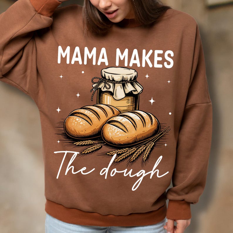 May include: Brown sweatshirt featuring the text "MAMA MAKES" above an illustration of two loaves of bread, a jar of honey, and wheat stalks. The text "The dough" is written below the illustration.