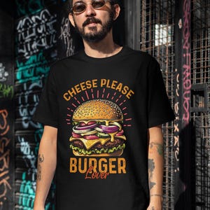 Pu&ograve; includere: Una maglietta nera con una grafica di un cheeseburger e il testo "Cheese Please Burger Lover".