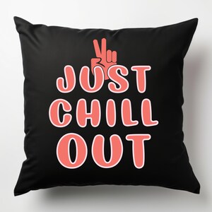 May include: Black square throw pillow with the words "JUST CHILL OUT" in coral-colored letters. A coral-colored hand in a peace sign is above the text. The pillow is a decorative item.