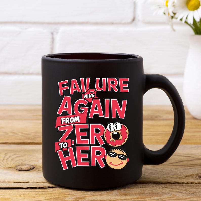 May include: Black ceramic mug with a humorous design in red and white. The text reads "Failure Wins Again From Zero to Hero" with cartoon donut and face graphics. The mug is on a wooden surface.
