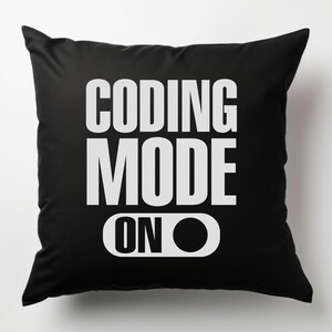 Puede incluir: Coj&iacute;n negro con las palabras "CODING MODE ON" en blanco, en negrita y sin serifa. El texto est&aacute; dispuesto en tres l&iacute;neas, con "ON" como un gr&aacute;fico de interruptor.