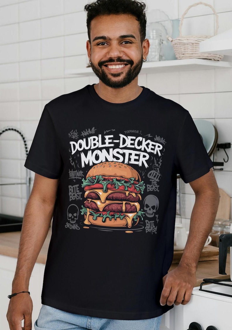Pu&ograve; includere: Maglietta nera con una grafica di un grande hamburger a due piani con il testo "Double-Decker Monster" in bianco. L'hamburger ha lattuga, pomodoro, formaggio e due hamburger di manzo. La grafica &egrave; circondata da testo in stile graffiti e teschi.