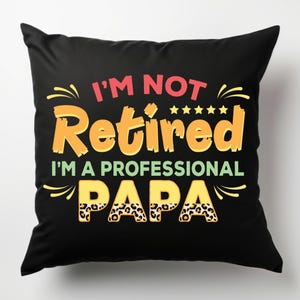 Może przedstawiać: Czarna kwadratowa poduszka z napisem "I'M NOT Retired I'M A PROFESSIONAL PAPA" w kolorze czerwonym, pomarańczowym, ż&oacute;łtym i zielonym. Słowo "PAPA" ma wz&oacute;r w panterkę. Zawiera dekoracyjne gwiazdki i ozdoby.
