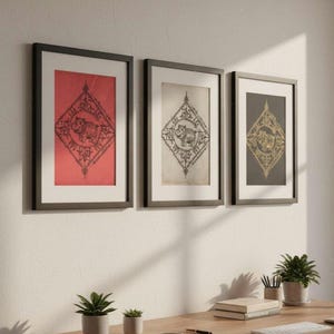 Peut inclure: Trois impressions encadrées avec des cadres noirs sont accrochées à un mur blanc. Chaque impression présente un motif symétrique détaillé avec une figure centrale. Les fonds sont rouges, blanc cassé et gris foncé. Un bureau en bois avec des plantes et des fournitures de bureau est au premier plan.