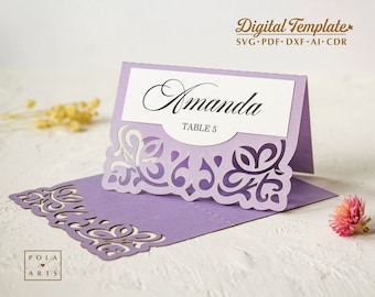 Könnte beinhalten: Lilafarbene Tischkarten aus Laser-geschnittenem Papier mit einem dekorativen Design und dem Namen "Amanda" und "Tisch 5" darauf gedruckt.