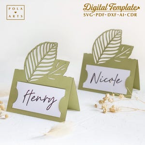 Può includere: Due porta biglietti da visita verdi con un design a foglia. I biglietti da visita sono vuoti e pronti per essere personalizzati con i nomi. Il testo sui biglietti da visita recita "Henry" e "Nicole".