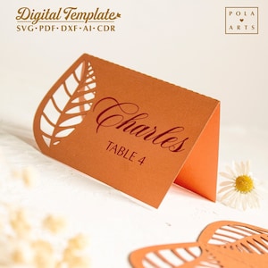 May include: Orange table number card with a cut-out leaf design. The card says "Charles" and "Table 4" in a red script font.