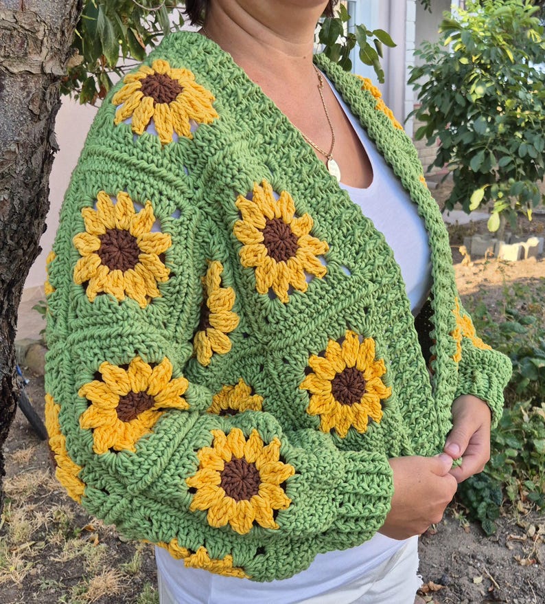 May include: A green crocheted cardigan with a sunflower pattern. The cardigan has a V-neck and long sleeves.