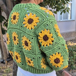 May include: Green crochet cardigan with a sunflower pattern. The cardigan has long sleeves and a cropped length.