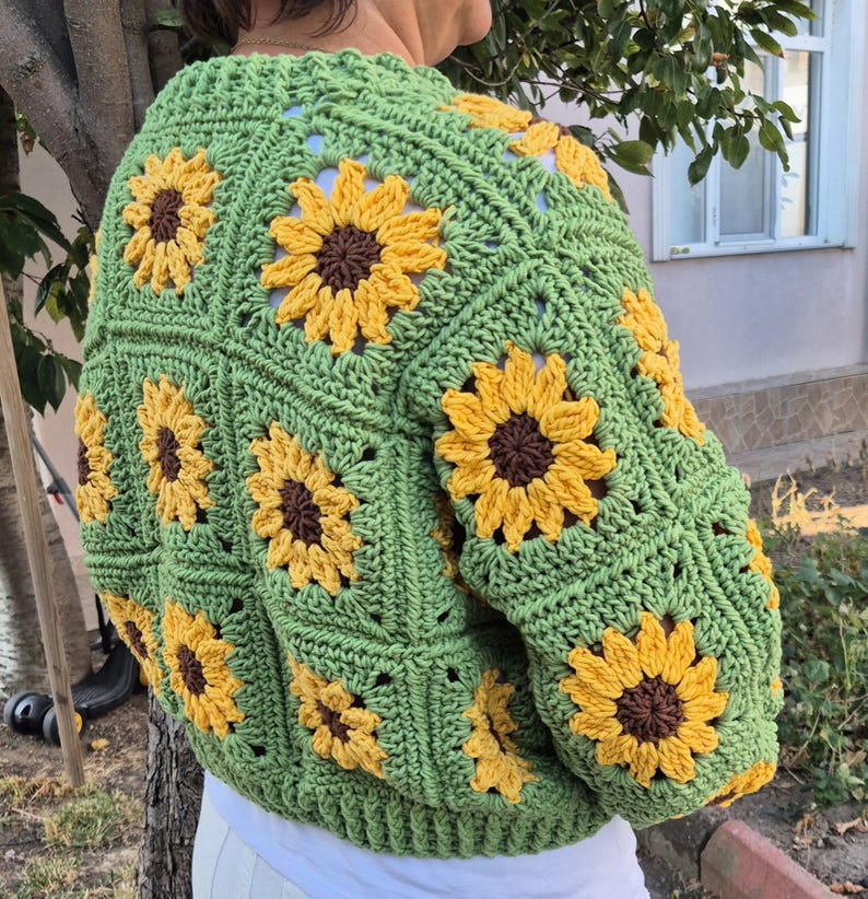 May include: Green crochet cardigan with a sunflower pattern. The cardigan has long sleeves and a cropped length.