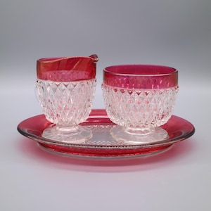 May include: A vintage cranberry glass creamer and sugar bowl set with a diamond pattern and a matching tray.