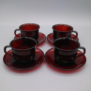 Può includere: Set di quattro tazze da tè e piattini in vetro rosso. Le tazze e i piattini sono di un colore rosso intenso e ricco e hanno una finitura lucida.