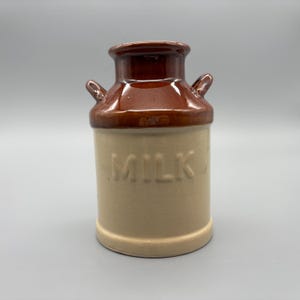 Peut inclure: Pichet à lait en céramique avec un dessus et des poignées marron et une base beige. Le mot "MILK" est en relief sur le devant. Le pichet a un design classique et vintage.