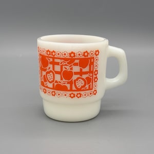 Puede incluir: Una taza de cerámica blanca con un diseño apilado. La taza presenta un vibrante patrón de manzanas y flores de color naranja. El asa es de color blanco liso. La taza es de tamaño estándar para café o té.