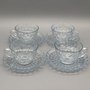Puede incluir: Cuatro tazas y platillos de té de vidrio transparente. Cada taza y platillo tiene un patrón texturizado similar a burbujas. Las tazas tienen asas y los platillos son redondos con un borde festoneado.