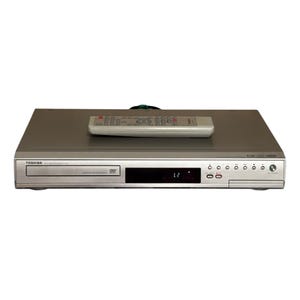 May include: Silver Toshiba DVD player with a matching remote control. The DVD player has a disc tray, a display screen, and several buttons. The remote control is white with numerous buttons. The DVD player is on a white background.