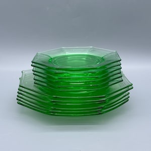 Könnte beinhalten: Ein Stapel grüner Glasplatten mit achteckiger Form. Die Teller haben eine leuchtend grüne Farbe und scheinen aus der Vintage-Ära zu stammen. Die Teller sind übereinander gestapelt, mit ein paar Tellern im Vordergrund.