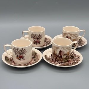 Könnte beinhalten: Vier Vintage-Tassen und Untertassen. Die Tassen und Untertassen sind cremefarben mit braunen und roten Blumen- und Landschaftsmotiven. Die Tassen haben Henkel und stehen auf passenden Untertassen. Das Set steht vor einem hellgrauen Hintergrund.