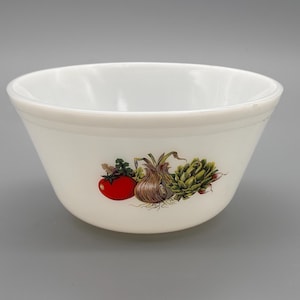 May include: White ceramic bowl with a colorful vegetable design. The bowl features a red tomato, a brown onion, and a green artichoke. The bowl is round and has a slightly flared shape, suitable for serving or food preparation.