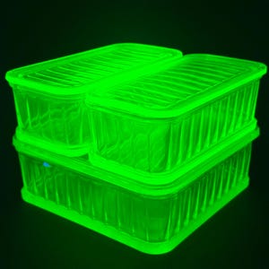 Puede incluir: Tres recipientes rectangulares de vidrio con tapas a juego, que brillan con una fluorescencia verde neón brillante. Cada recipiente presenta un patrón acanalado vertical en los lados y una textura acanalada horizontal en la tapa, apilados.
