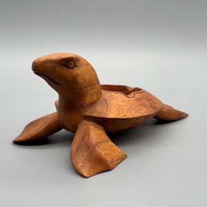Puede incluir: Figura de tortuga de madera tallada a mano con acabado marrón. La tortuga tiene una hendidura en forma de cuenco en la espalda y la cabeza levantada. Las aletas están extendidas. Este artículo decorativo es adecuado para la decoración del hogar.
