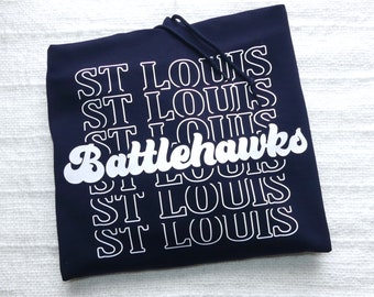 Puede incluir: Una sudadera con capucha azul marino con el texto "ST LOUIS" repetido cinco veces y el texto "Battlehawks" en una fuente blanca estilizada.