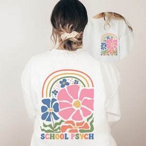 May include: White long-sleeved sweatshirt with a rainbow and flower design on the back. The text "SCHOOL PSYCH" is printed below the design.