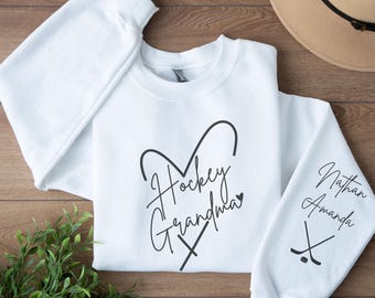May include: White sweatshirt with a black heart design that says "Hockey Grandma" and two crossed hockey sticks. The sleeve has the names "Nathan" and "Amanda" written in black with two crossed hockey sticks.