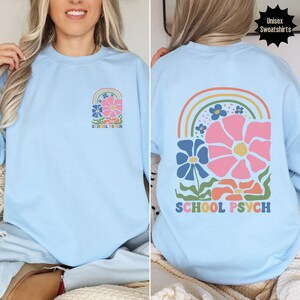 May include: Light blue sweatshirt with a rainbow and flower design. The text "SCHOOL PSYCH" is printed on the front and back of the sweatshirt.