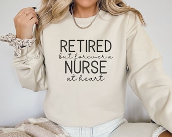 May include: A beige sweatshirt with the text "Retired but forever a Nurse at heart" printed in black.